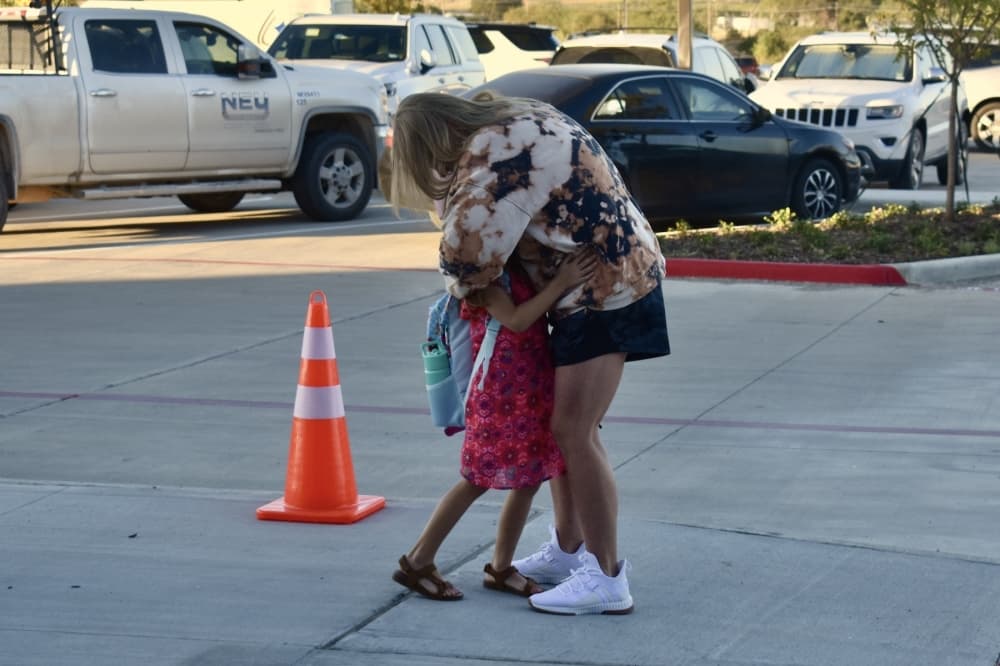 a young child and adult hug outside of school