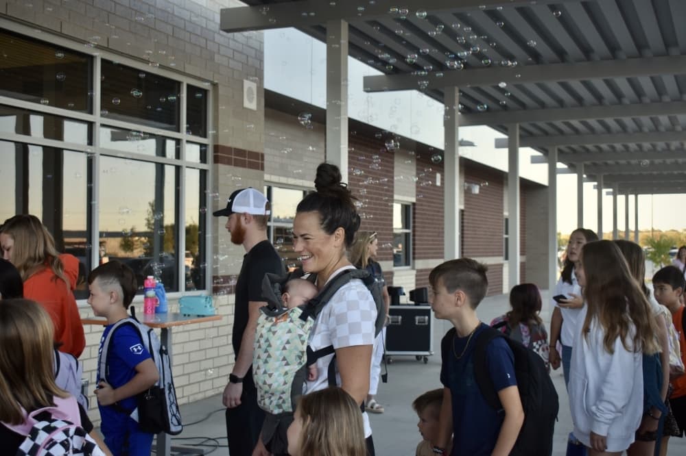 a mother with a baby on her chest walks her kids into a school