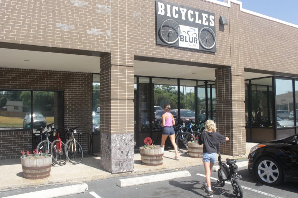 The exterior of Blur Cycleworks, a woman and her child walk into the store with a scooter