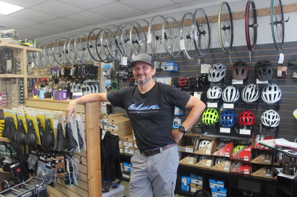 Blur Cycleworks owner Eric Warnsman poses inside the bike shop next to helmets and bike seats