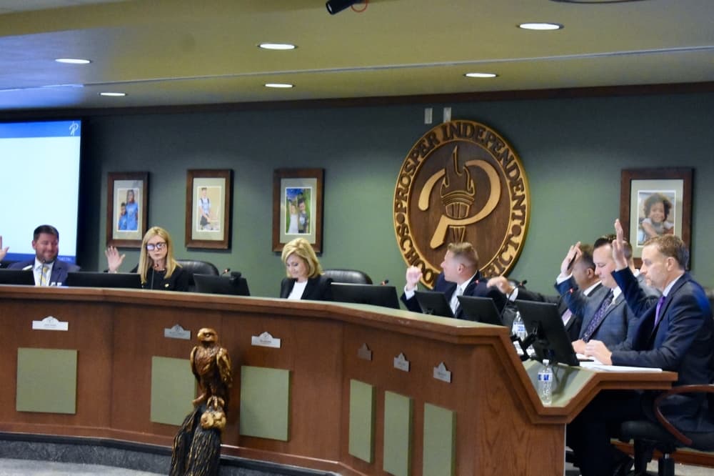 people behind a large desk raise their hands at a school board meeting