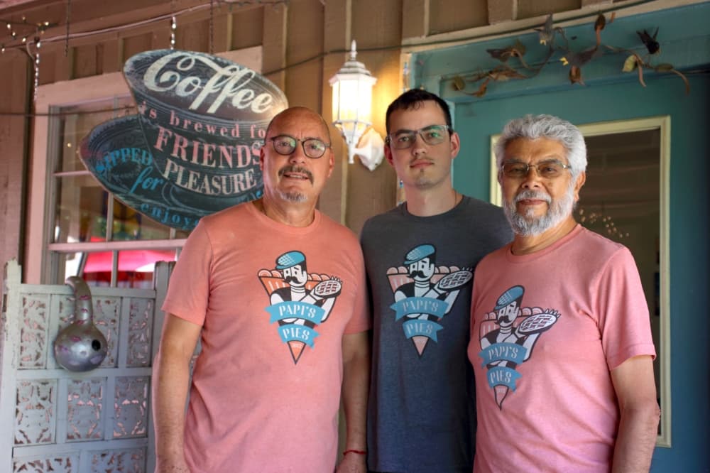 three men standing outside a restaurant in pink or gray T-shirts