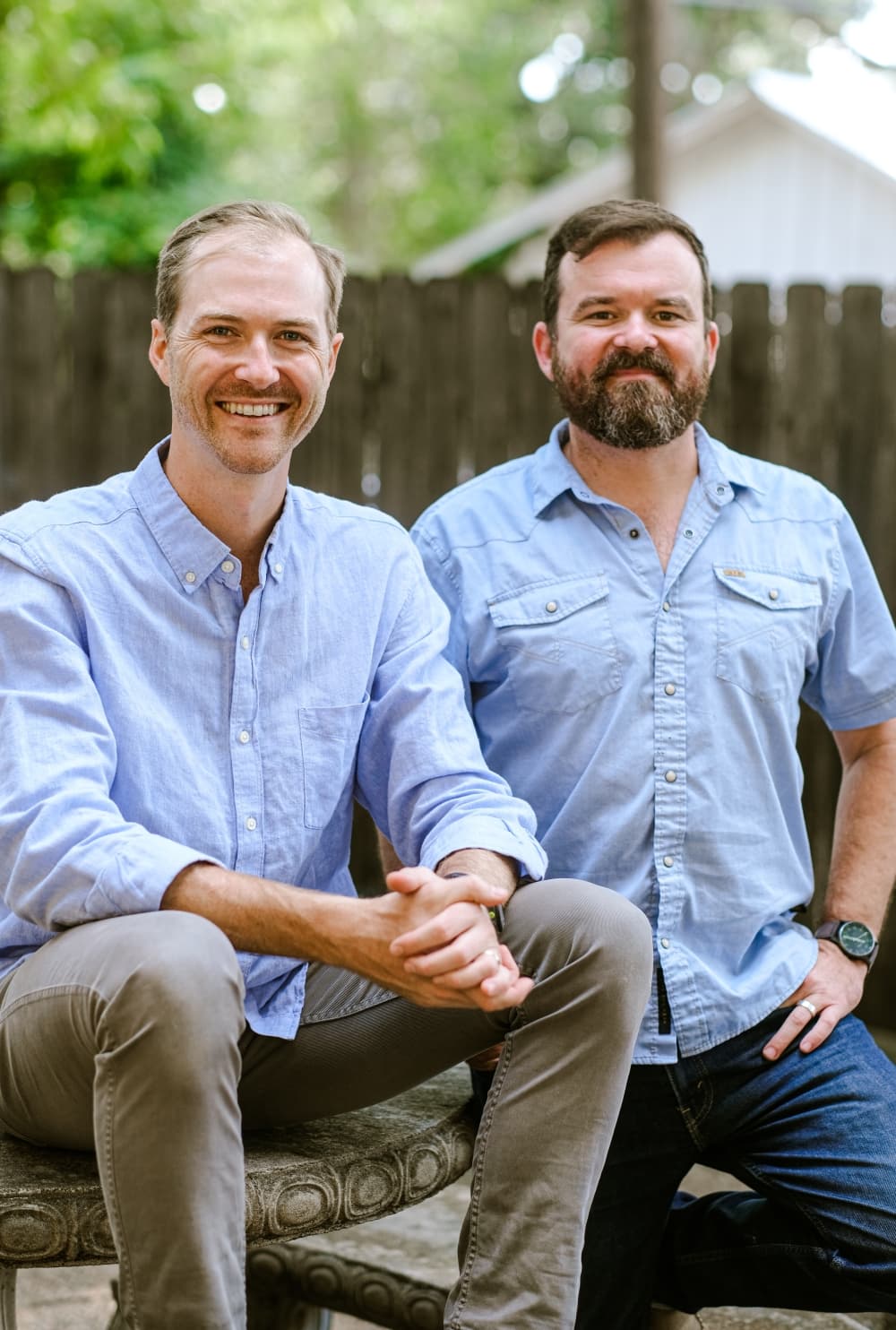 Two men pose for a photo outside on a sunny day.