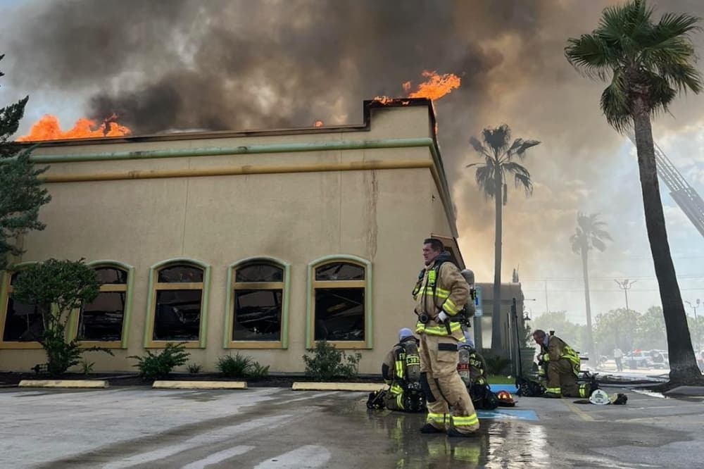 The photo shows the Los Cucos restaurant on fire with a firefighter standing out front.