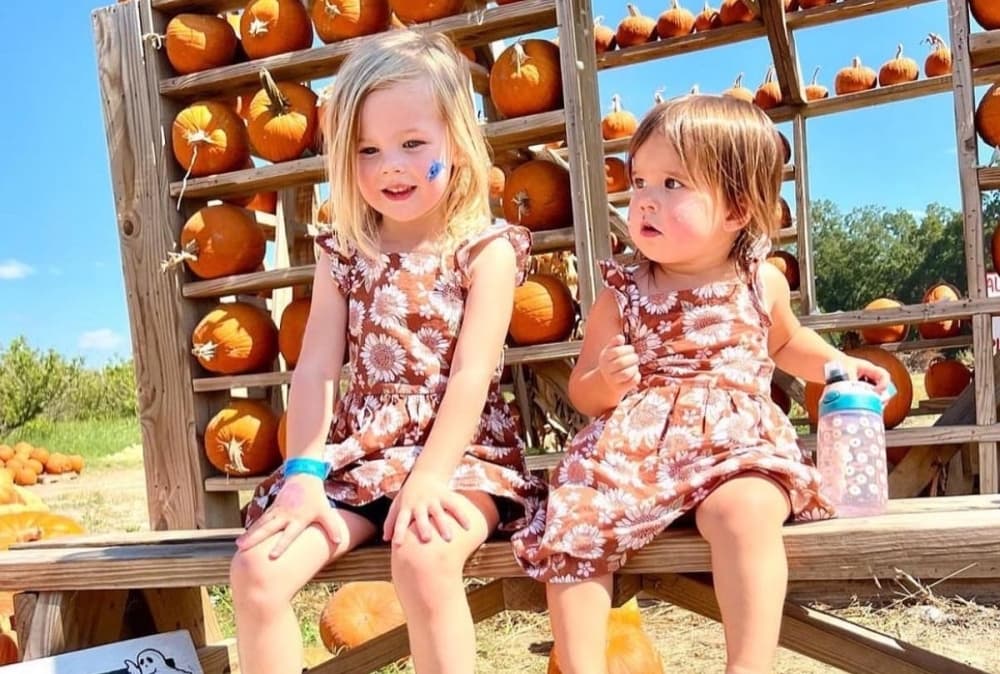 Two children pose in front of some pumpkins at the farm outside.