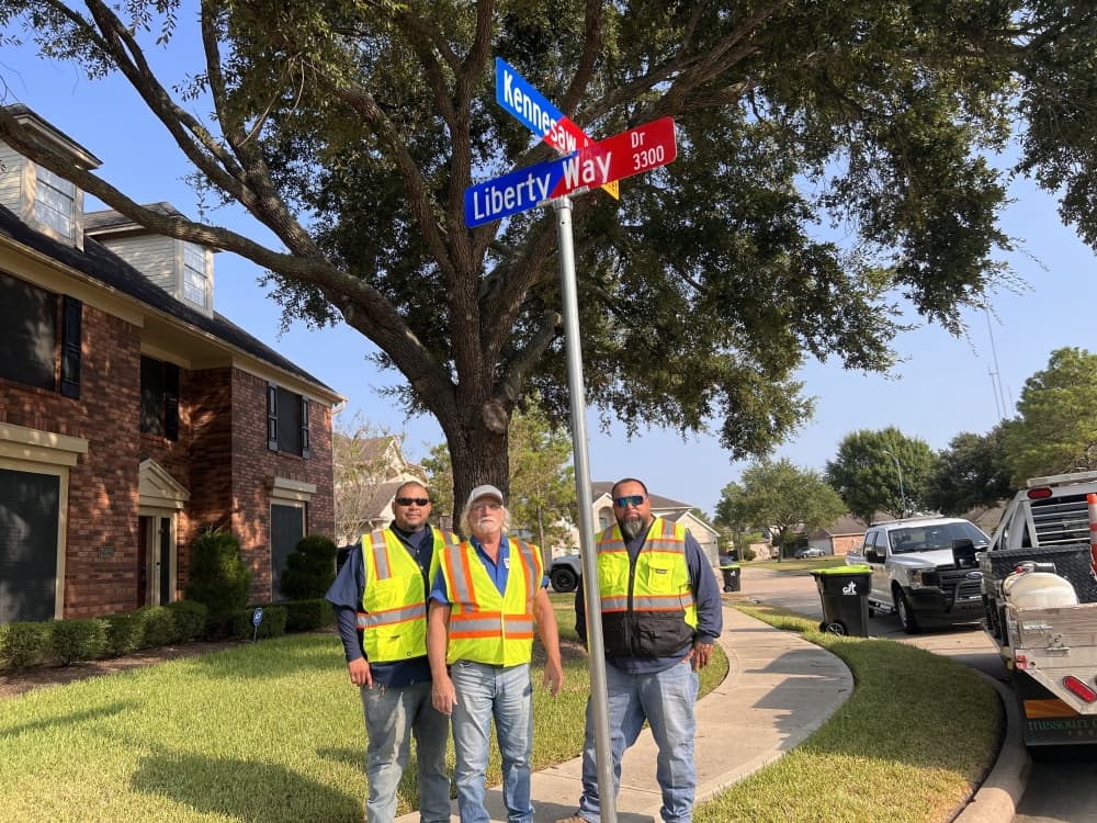 3 construction workers standing under a newly installed street sign reading "Liberty Way"