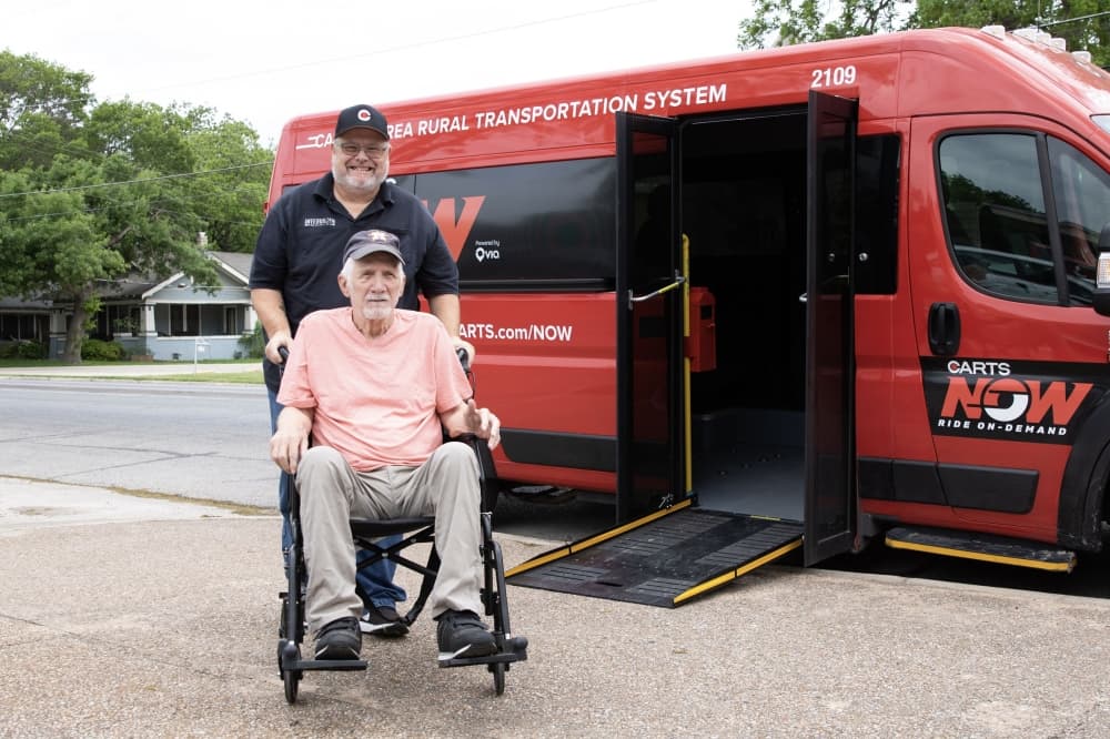 A middle-aged man and a man in a wheelchair in front of a CARTS Now bus.