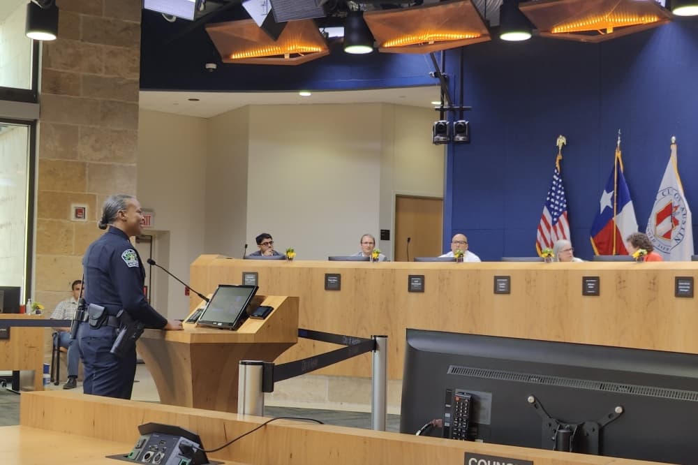 city council members sit behind the dais while robin henderson stands at a podium in front of them