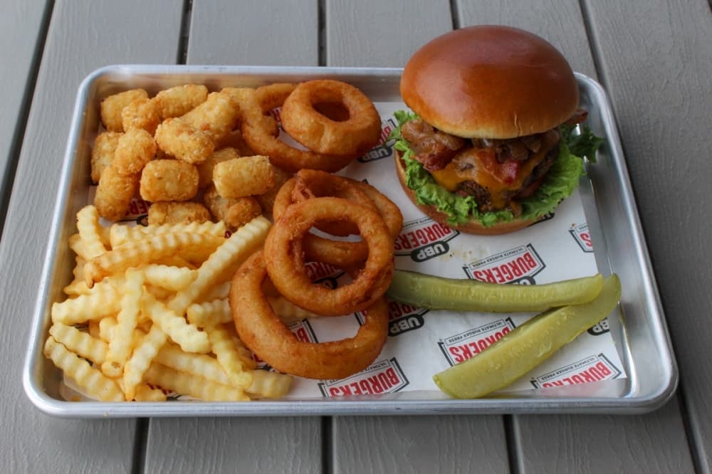 a tray with a burger, pickles, tater tots, fries and onion rings as side options for their burgers. 