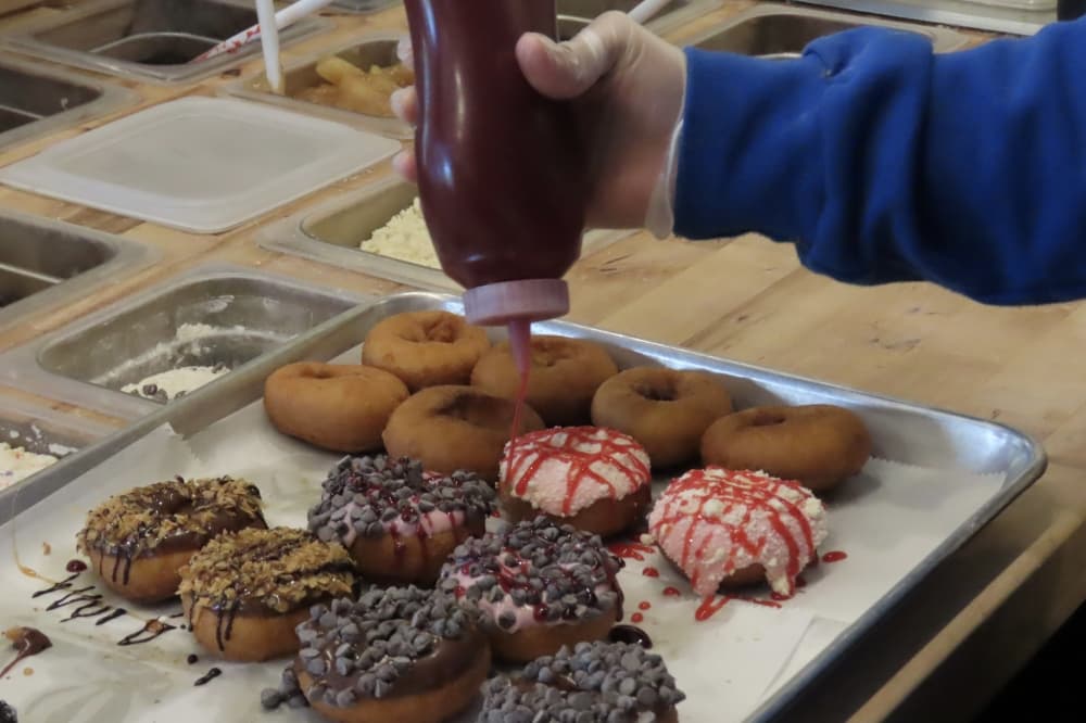 Employee drizzles sauce onto cake doughnuts at Peace, Love and Little Donuts in Southlake. 