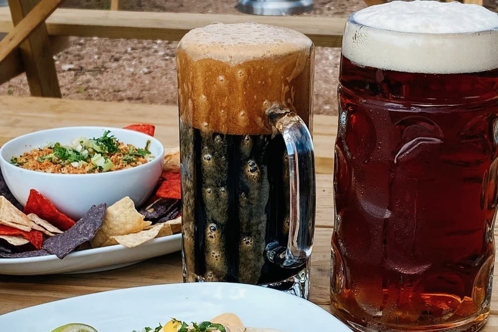 Two pitchers of beer on a table next to chips and salsa