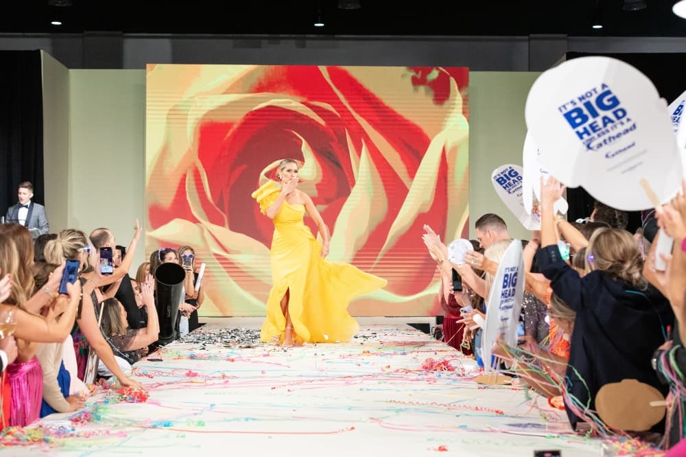 A woman walks down a runway in a yellow dress.