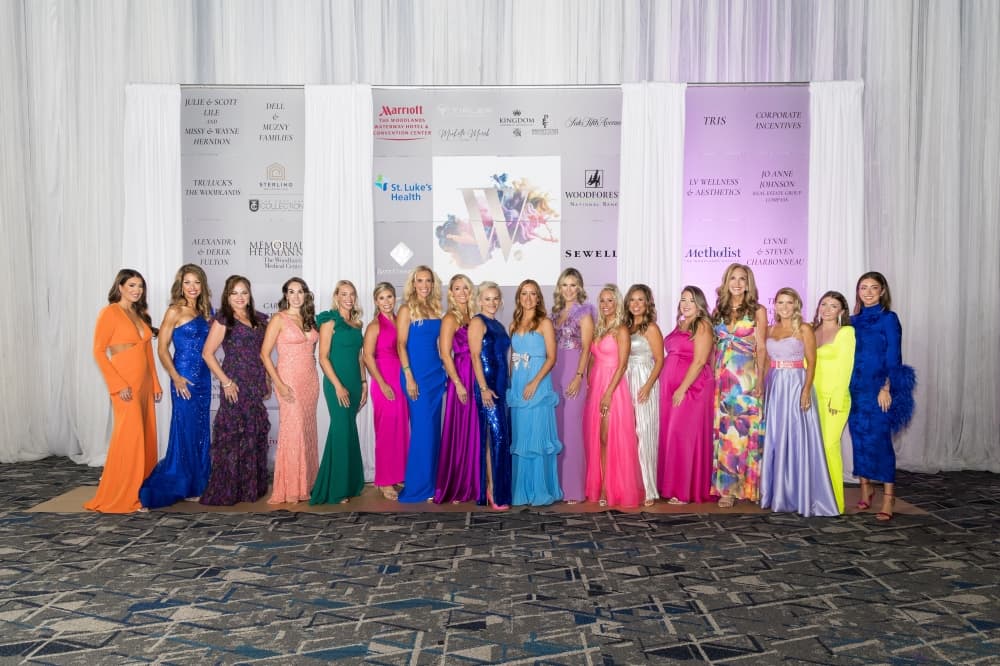 A group of about a dozen women in brightly colored dresses gather for a photo