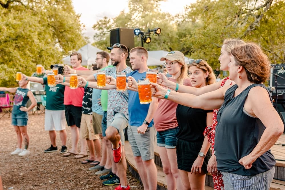 A group of people hold up steins in a contest to see who can hold it up longest.