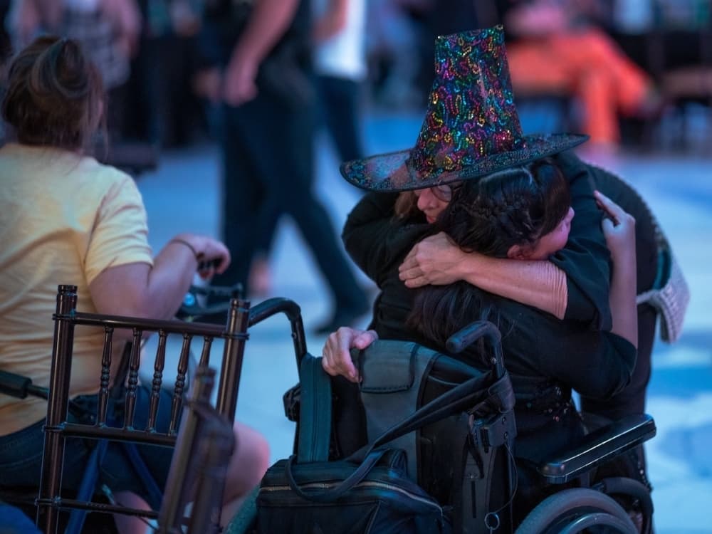 someone in a wheelchair hugs someone wearing a witch hat