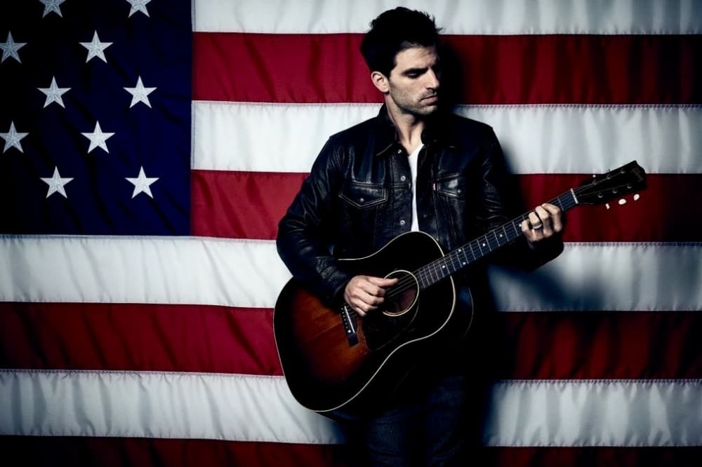 Mitch Rossell playing guitar with American flag in the background 