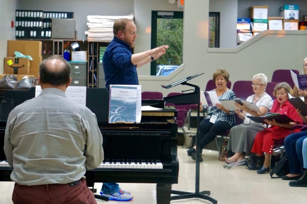 Guest director Jim Kritikos, standing, and assistant director Craig Stephan, on piano, direct a choir practice.