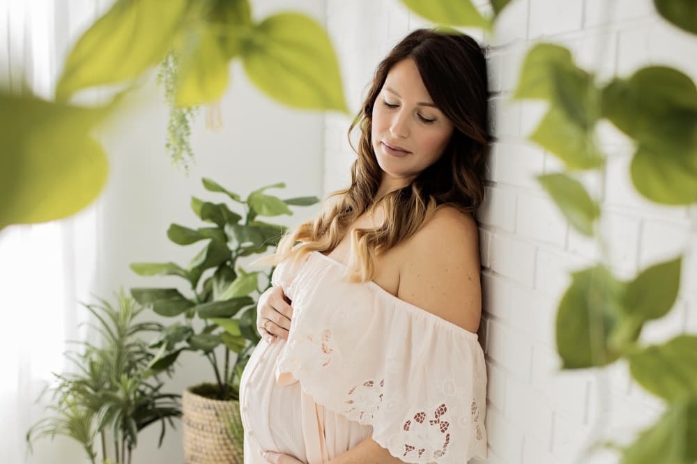 Maternity shoot with pregnant woman in white dress with green leaves in the background