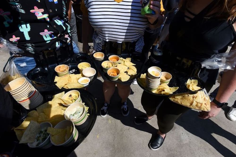 A group of people show off their plates of cheese goods outside on a sunny day.