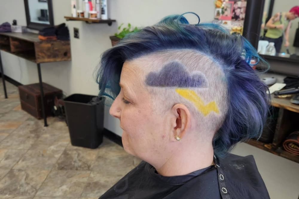 The photo shows a person with blue hair and a storm cloud shaved into their hair.