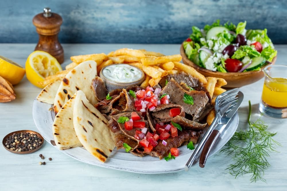 A plate of colorful Greek food rests on a table with accoutrements surrounding it.