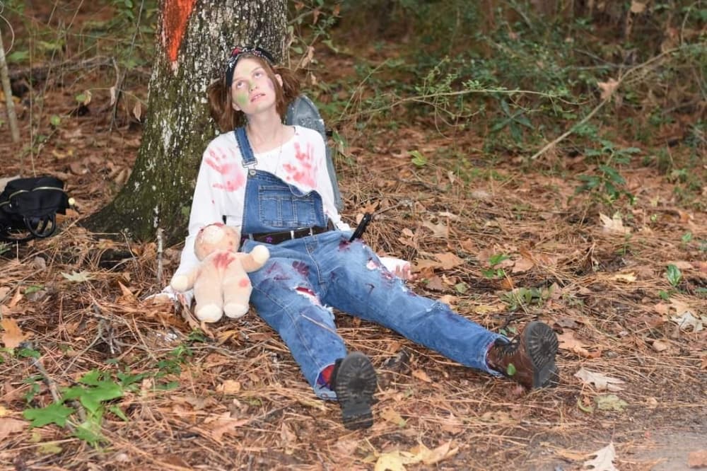 girl dressed as zombie playing dead under tree