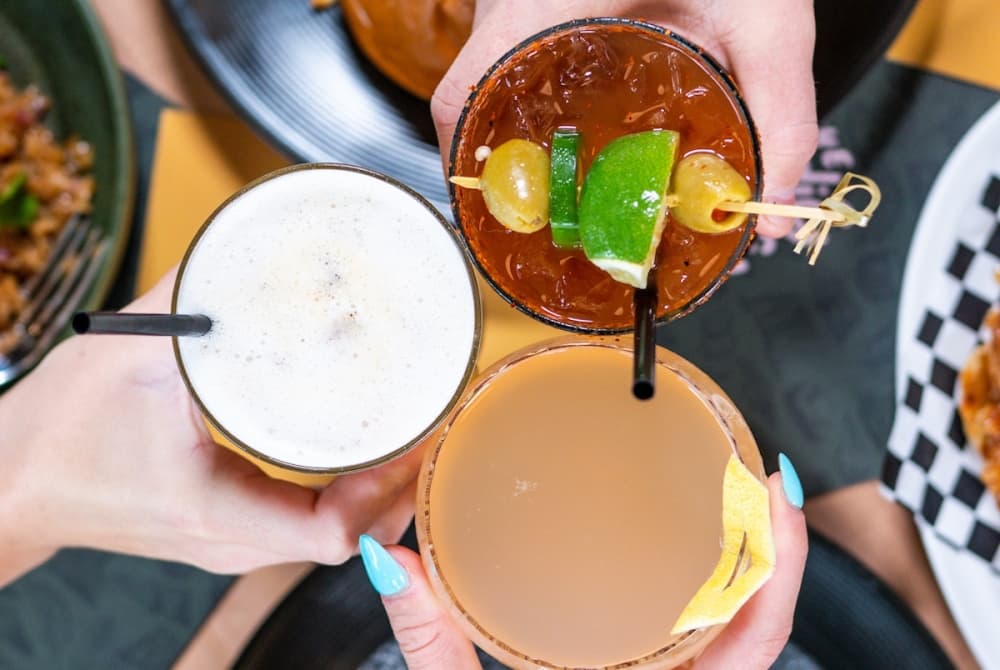 Three people toast one another with glasses of various drinks.
