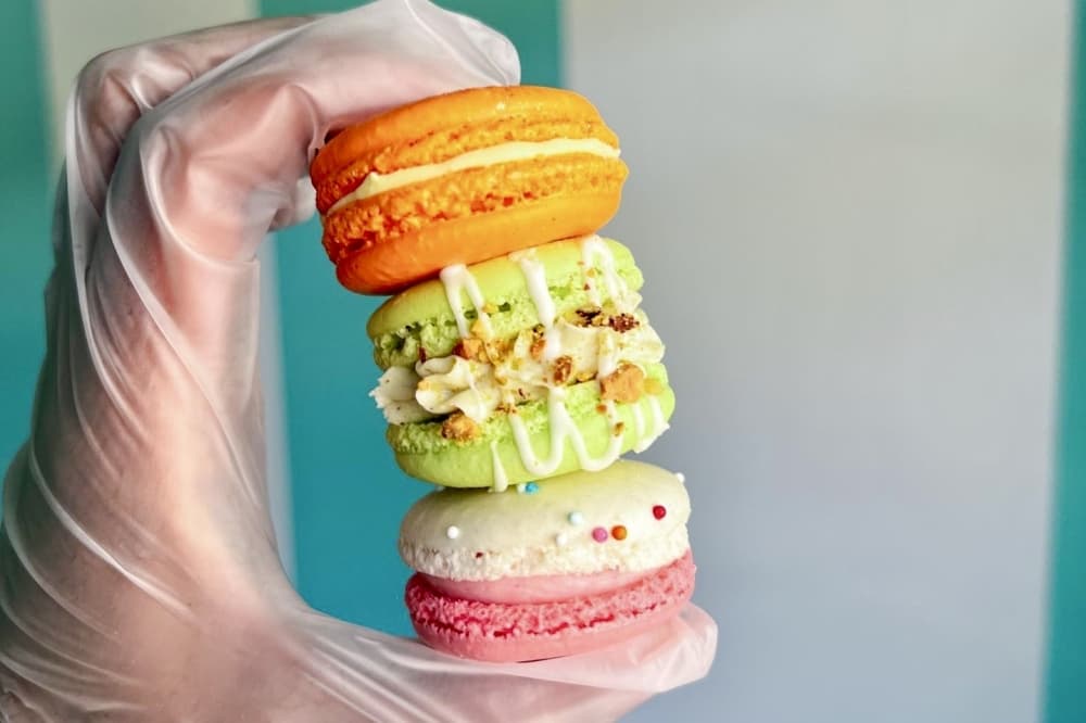 a hand in a food-handler's glove holding three macarons