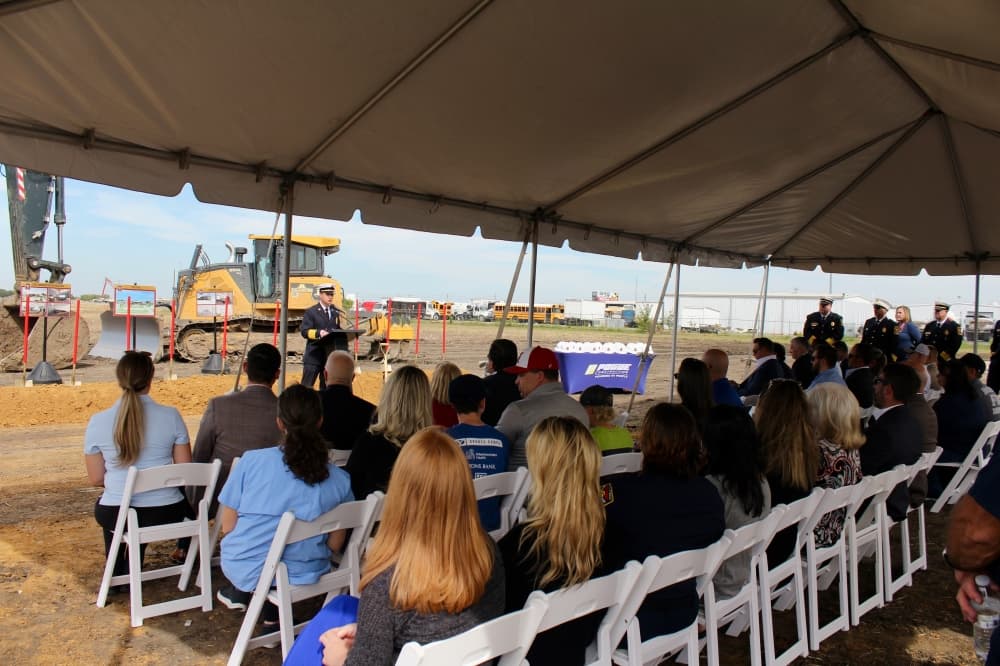 Groundbreaking event, crowd seated under a tent listening to a speaker