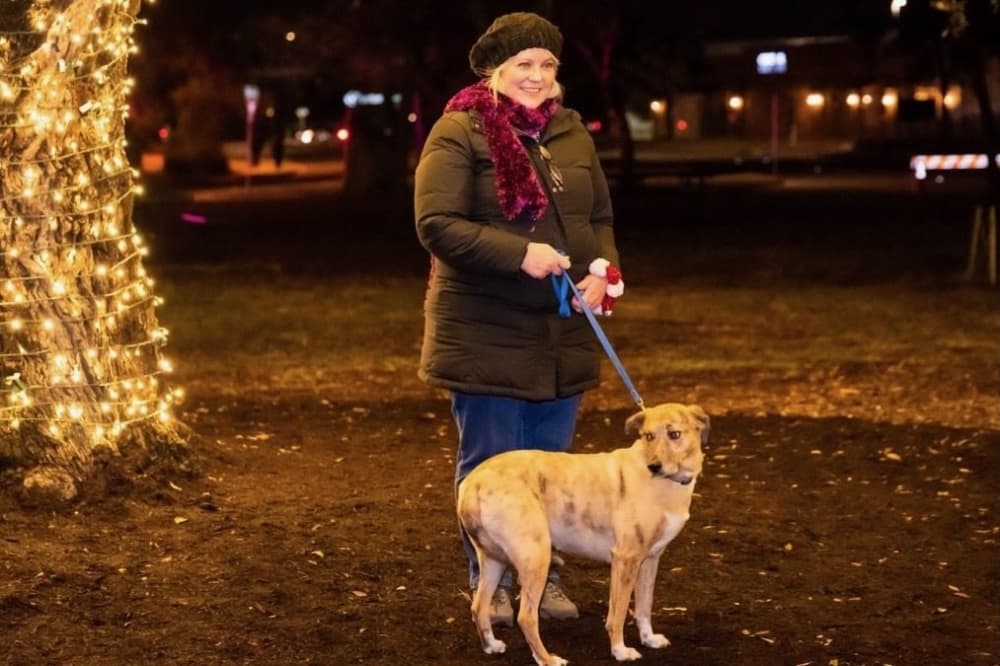 a woman and her dog outdoors, illuminated by the glow of holiday lights