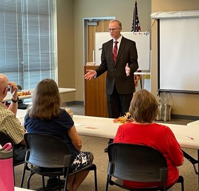 A man leads a presentation before adults in a classroom.
