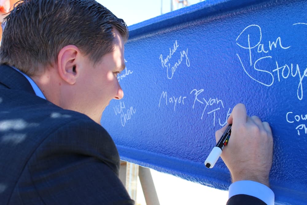 celina mayor ryan tubbs signing his name on a blue steel beam