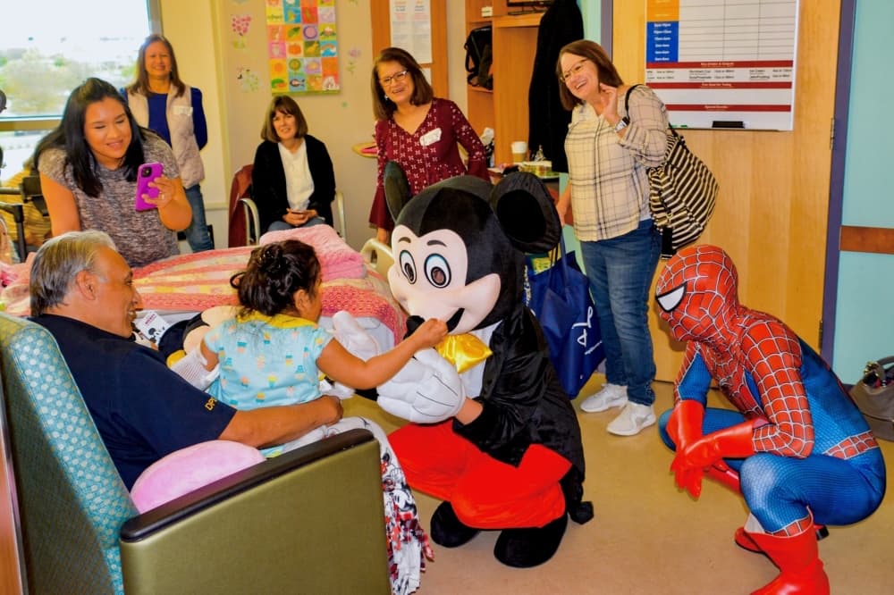 a child seated in someone's lap meets with Mickey Mouse and Spider-Man