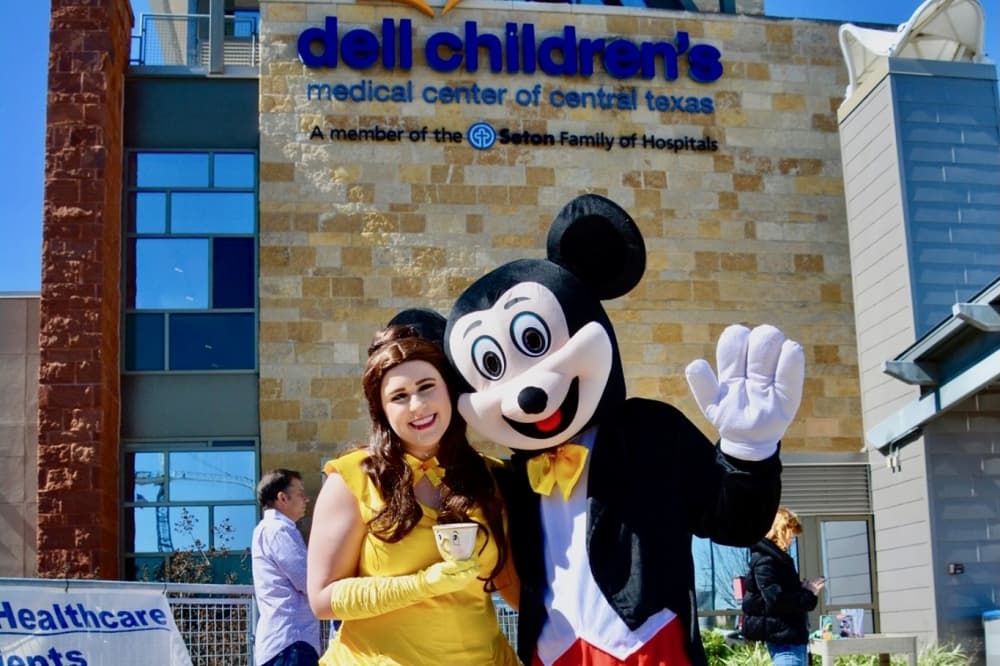 two people dressed as a princess and Mickey Mouse outside a hospital