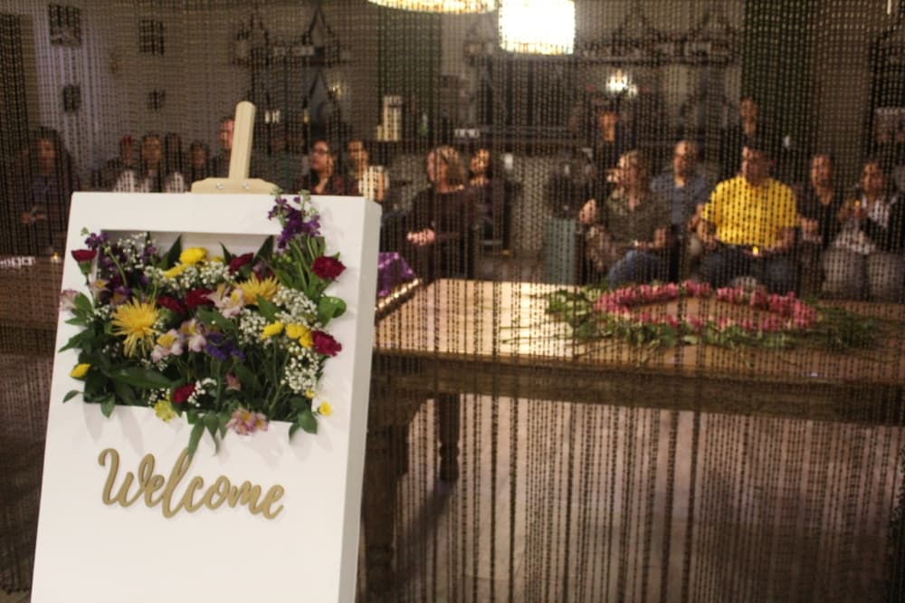 a welcome sign stands in front of a bead partition and seated guests