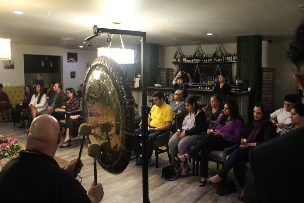 a man plays a gong in front of an audience seated in chairs holding candles