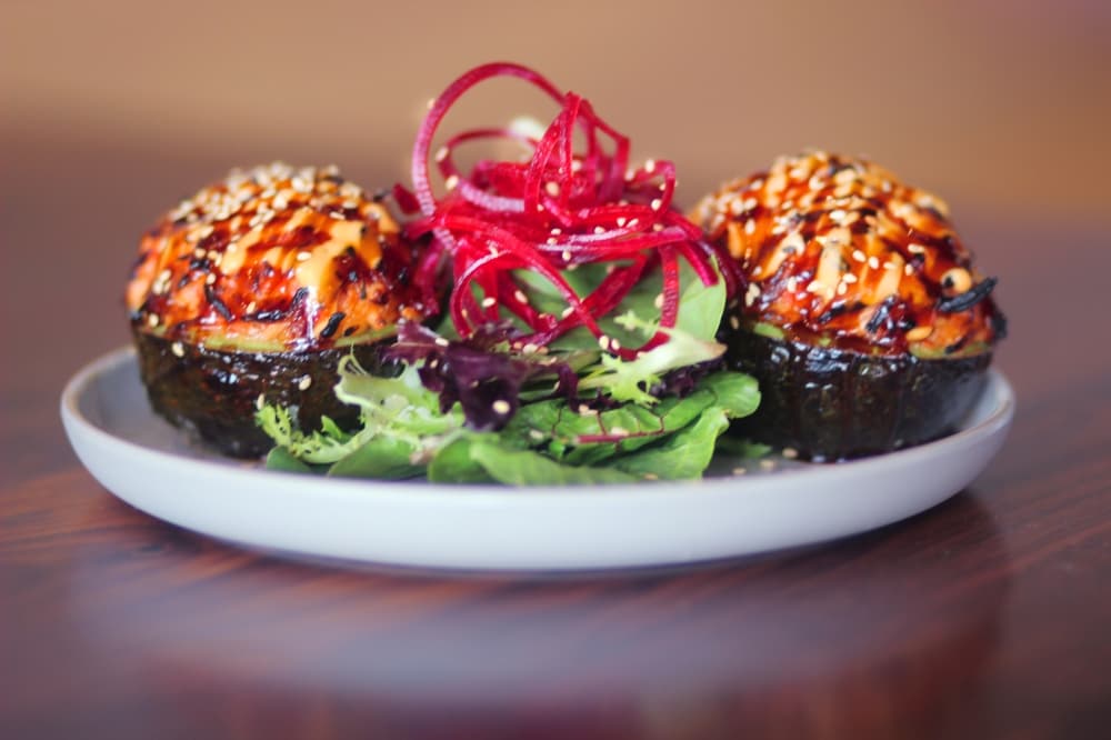 A white plate is filled with stuffed avocados and colorful vegetables.