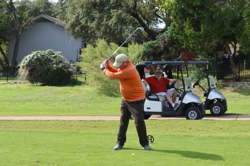 a golfer swinging while another golfer sits in a cart watching
