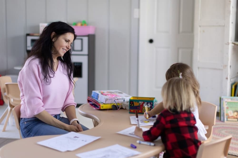 a woman watches two children coloring with markers