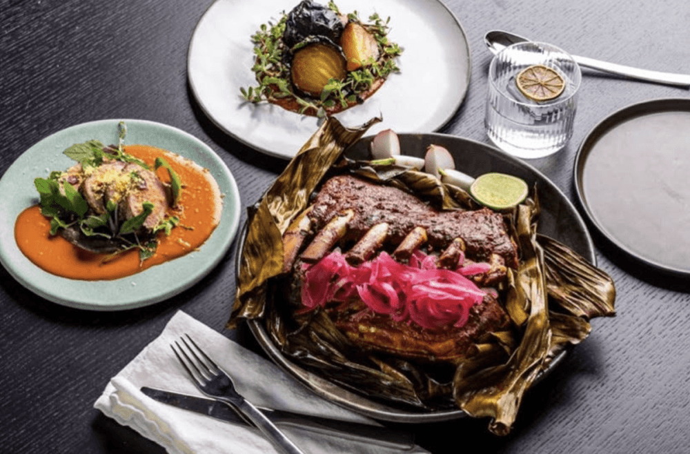 A table is filled with a pork shoulder roast and side plates with salsa and tortillas.