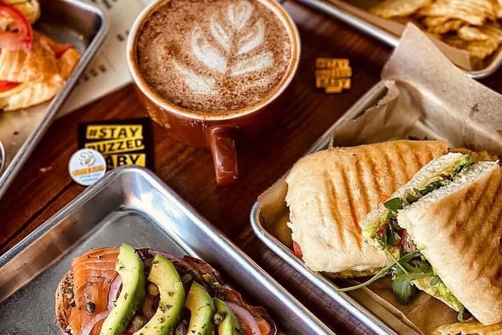 various food items on metal trays with a mug filled with coffee with latte art also pictured