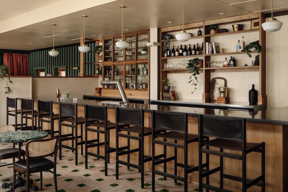 A look at the bar inside Poeta with black bar chairs, warm wooden colors and green plants.