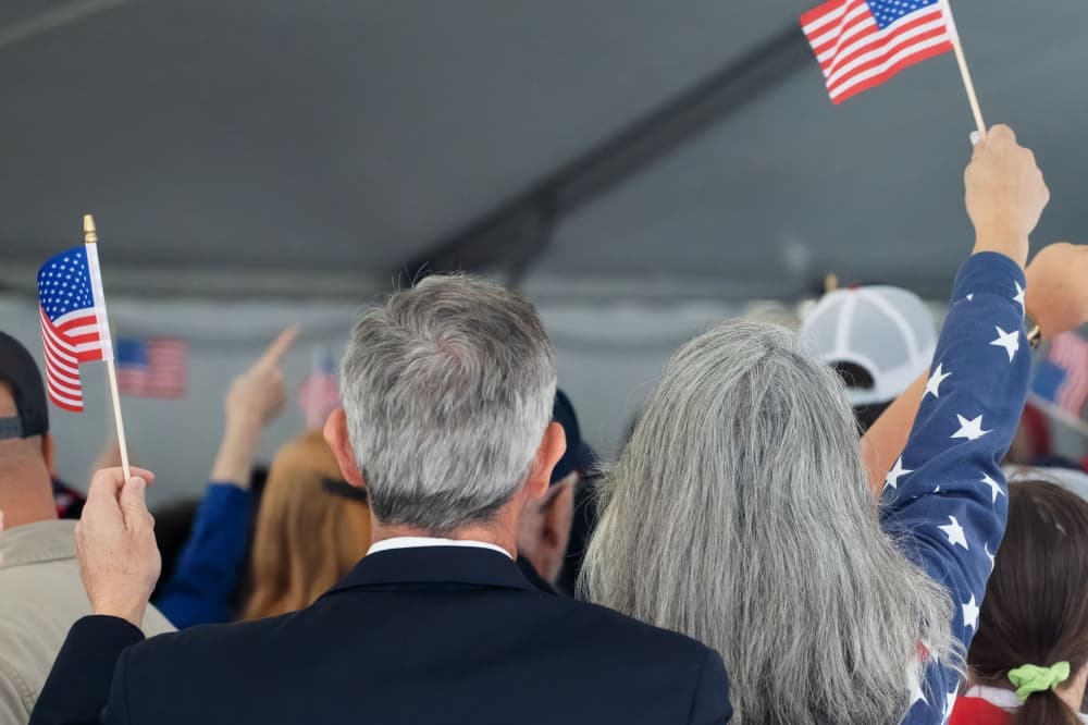 The backs of two people waving small American Flags