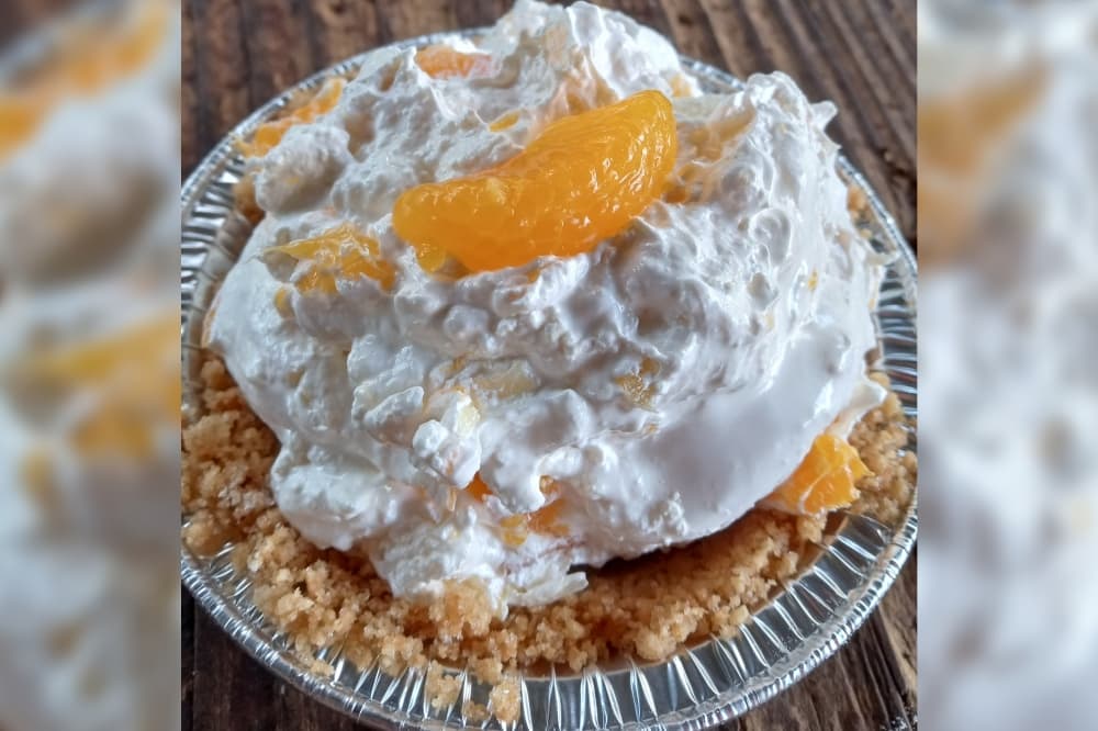 A small pie in a pie tin is pictured with whipped cream and a peach on top.