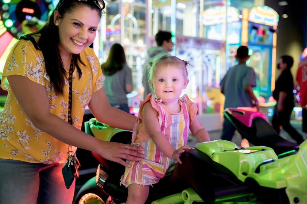 an adult holds a child that is on a motorcycle arcade game