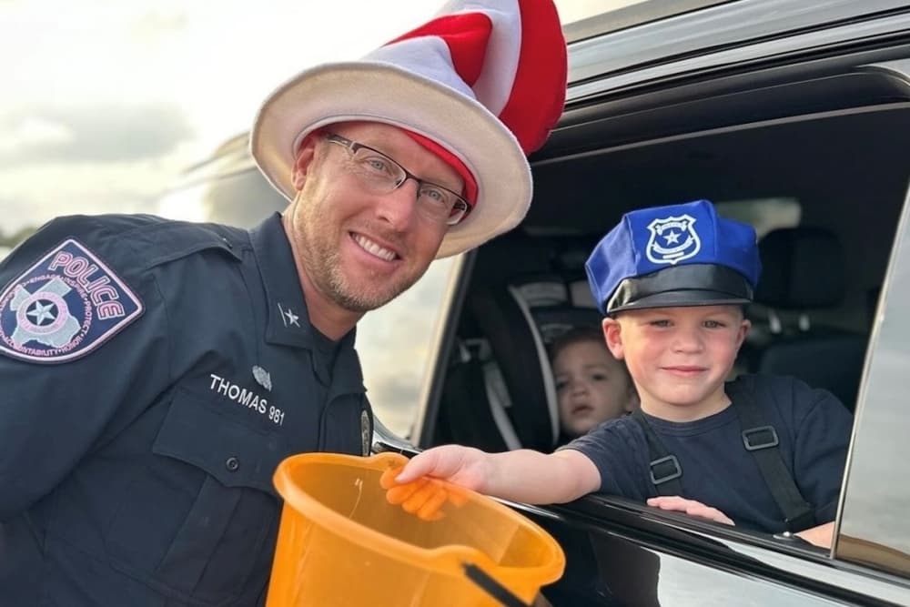A police officer wearing a Cat-in-the-Hat hat poses with a child holding an orange bucket and wearing a blue costume police hat.