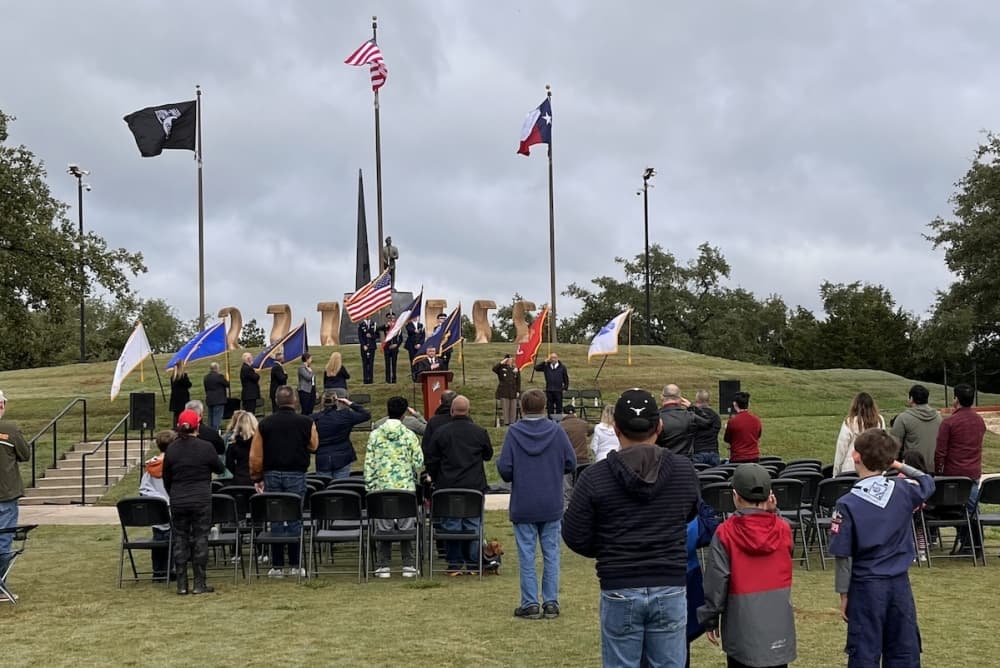 A group of people standing outside face the flags.