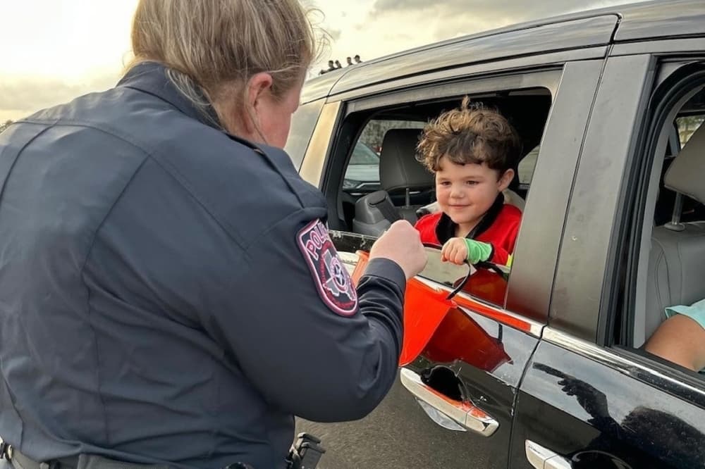 A police officer hands a child wearing a red shirt some candy.
