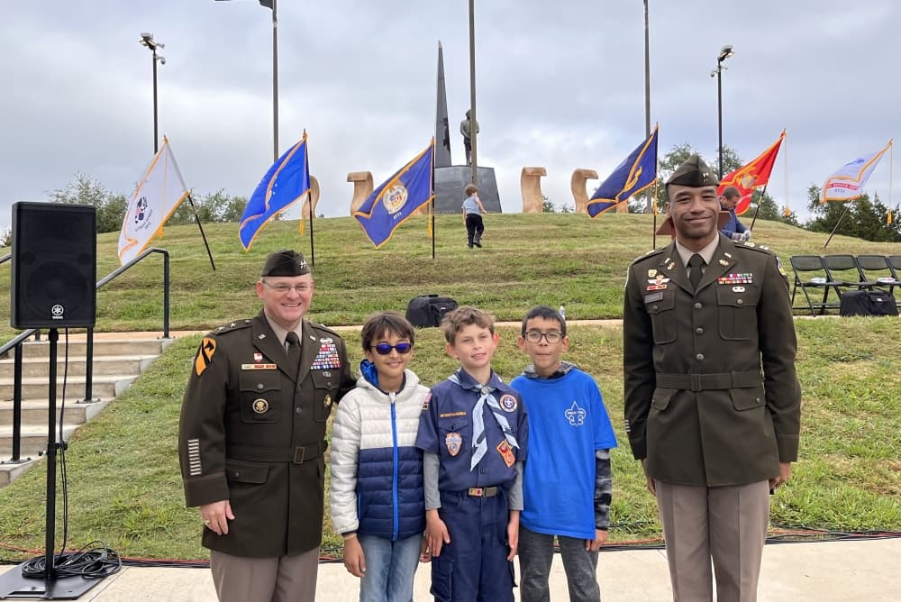 Three children pose for a photo with veterans outisde.