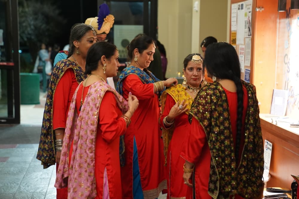 A group of women wearing red traditional Indian clothing help each other finish positioning their garments.